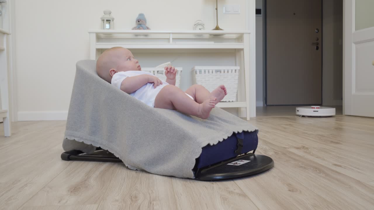 Robot vacuum cleaner performs automatic cleaning of apartment moves around baby in rocking chair, modern technology of smart cleaning.
