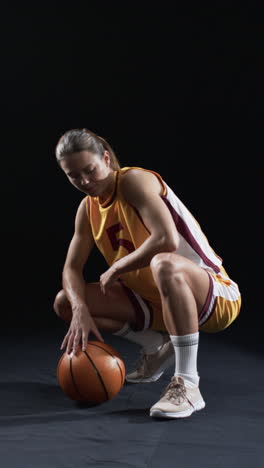 vertical video: caucasian female athlete with basketball in sportswear, black background