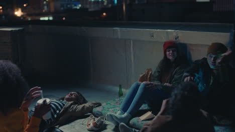 young group of friends relaxing on rooftop at night hanging out having casual conversation sharing snacks enjoying relaxing weekend party gathering