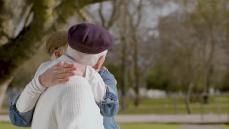 senior couple hugging while sitting on bench and spending time in park on sunny autumn day