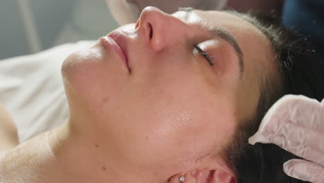 close up view of cosmetologist cleaning visitor face with cotton pads while visitor closes eyes peacefully during cosmetic spa treatment in bright clinic setting with soft lighting and ambient decor
