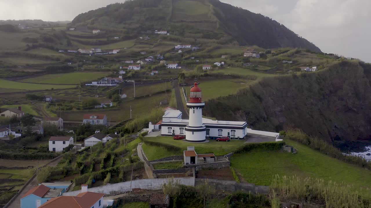 vista de drones de un faro en un pueblo costero rural, cielo nublado en topo, isla de são jorge, azores, portugal