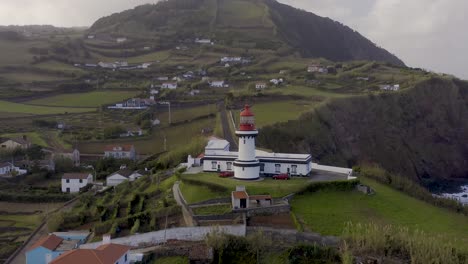 drone view of a lighthouse in an rural coastal village, cloudy sky in topo, são jorge island, the azores, portugal