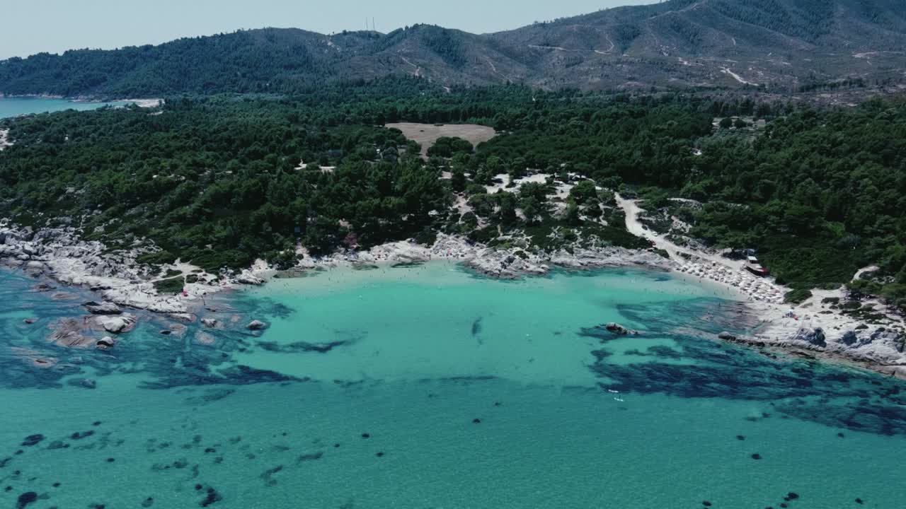 Aerial establishing shot of crystal clear water with many tourist swimming in bay on Chalkdiki, Greece