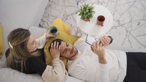 young couple hugging each other, talking while relaxing on sofa in modern home.