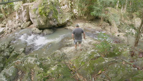 middle aged man climbs down rocks to fast flowing creek