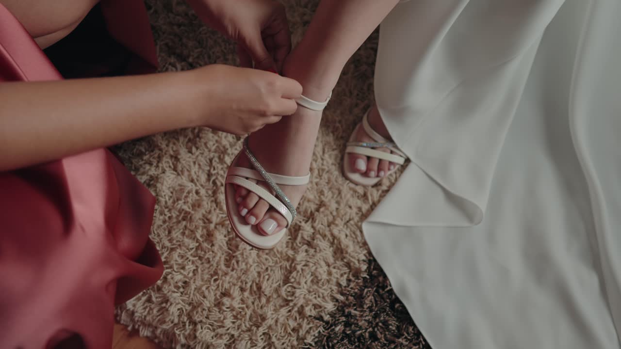 Close up of hands fastening white sandals on bride feet over carpet