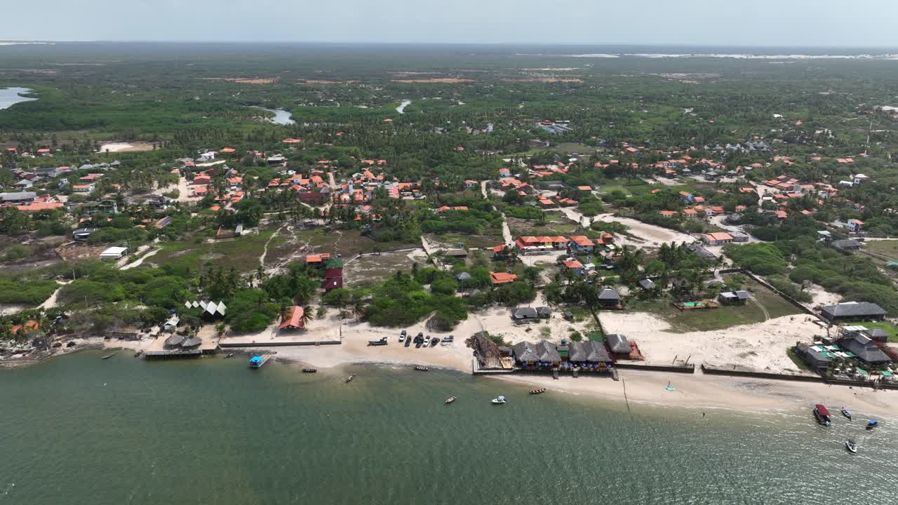 Aerial establishing overview of coastal village near white sand dunes in Lencois Maranhenses, Brazil, sprawling riverway and vegetation to horizon