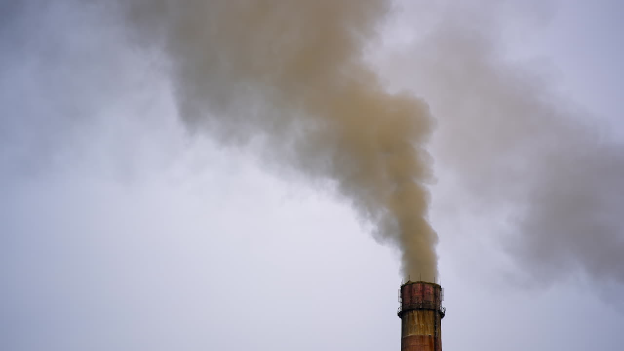 Smoking chimney against the grey sky. Air pollution. Thick smoke goes from industrial pipe. Ecological disaster. Harmful emissions fill the air in the evening.