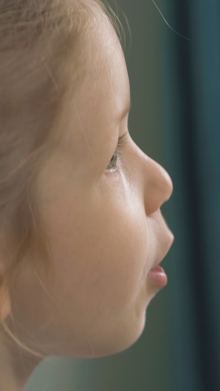 slow motion close up little girl play on electronic piano and sing sad song, with blond long hair gathered in pigtails, on background of blue curtains at home during self-isolation and epidemic