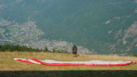 paragliders launch from grassy hillside with scenic mountain village view below