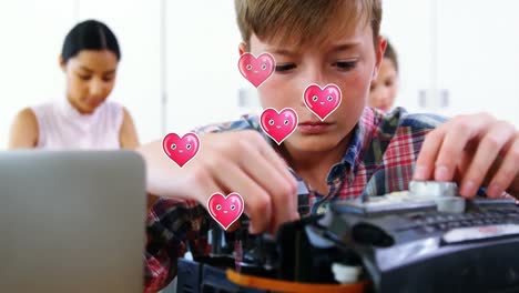 múltiples iconos de corazón rosa flotando sobre un niño caucásico reparando una computadora en la clase en la escuela