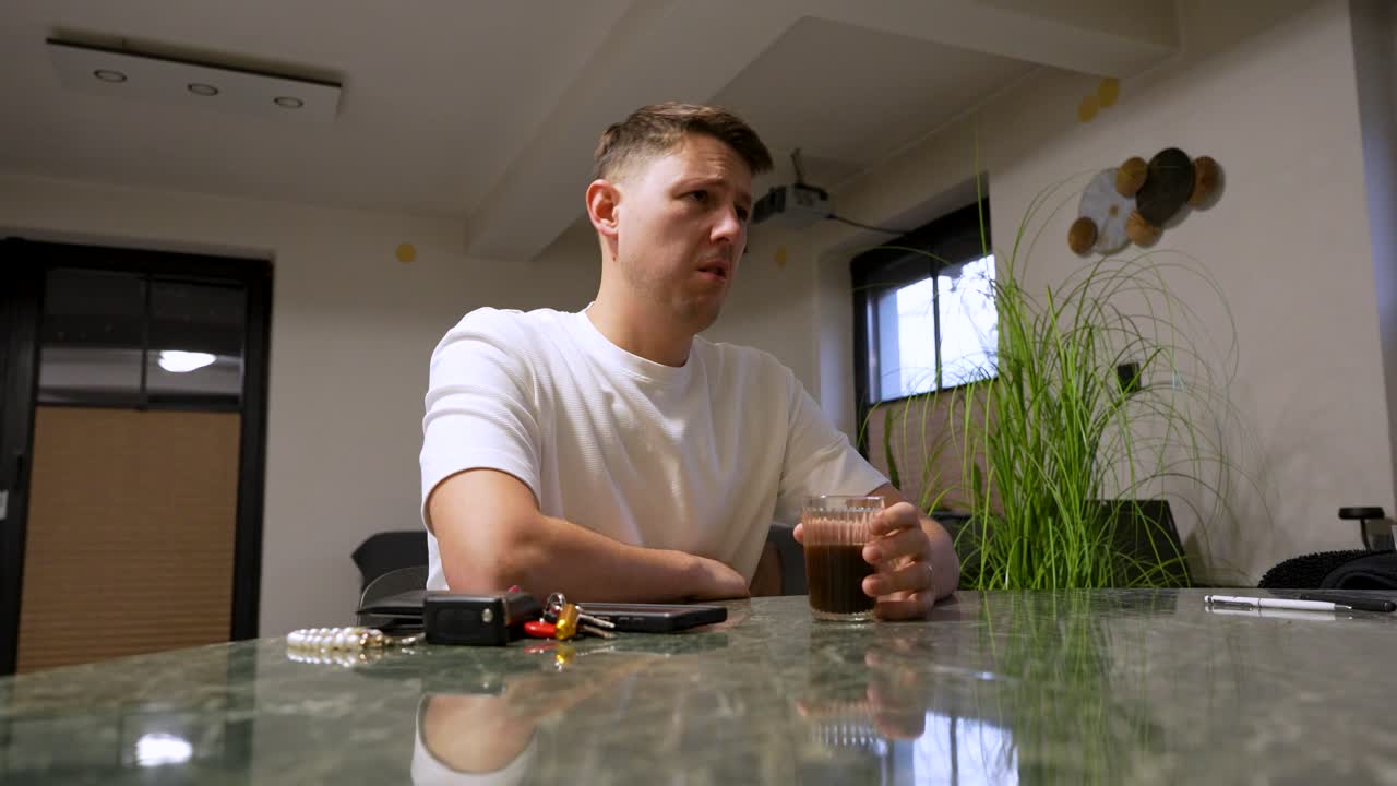 A man reacts with a disgusted facial expression while smelling and tasting burnt coffee in a modern kitchen, showing displeasure, surprise, and a strong negative reaction