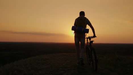 Ein-Mann-Mit-Rucksack-Und-Fahrrad-Steht-Und-Schaut-Auf-Den-Horizont,-Wo-Die-Sonne-Untergeht,-Radfahren-Und