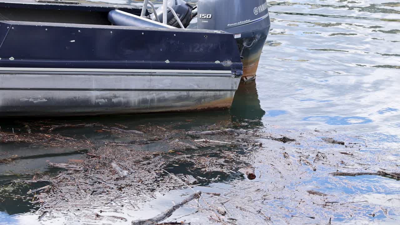 A stationary boat rests on calm waters in Queenstown, New Zealand, surrounded by floating debris under soft daylight