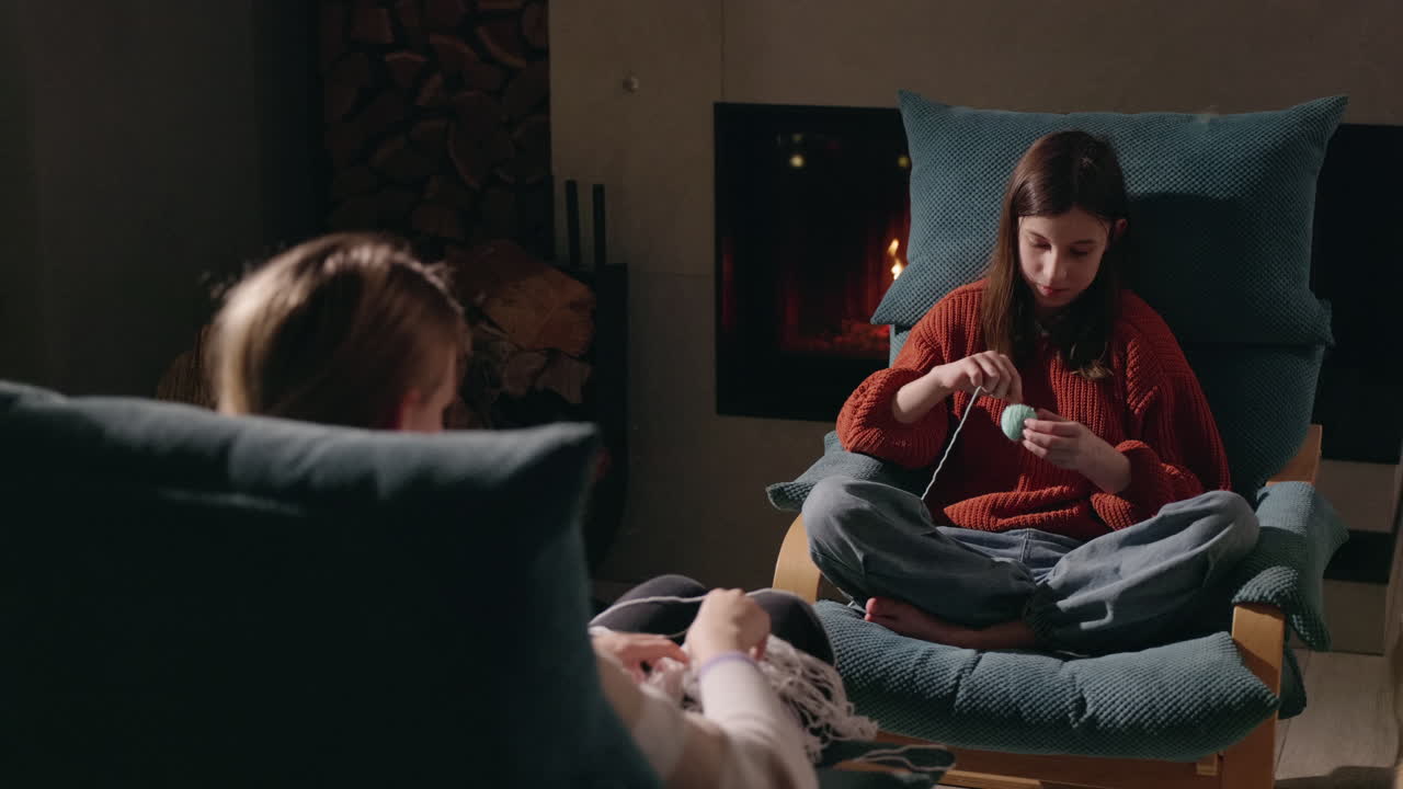 Two women knitting near fireplace