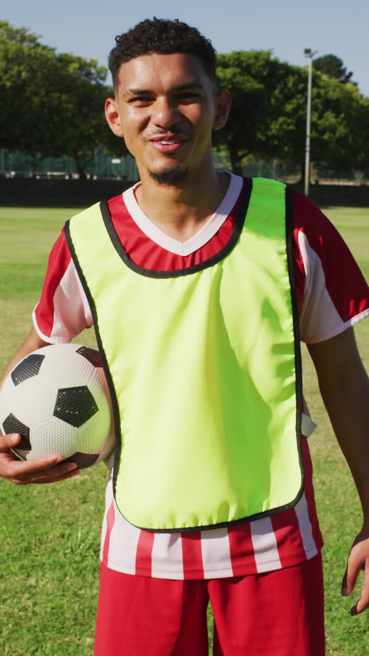 Video vertical de un jugador de fútbol americano birracial en el campo con un balón.