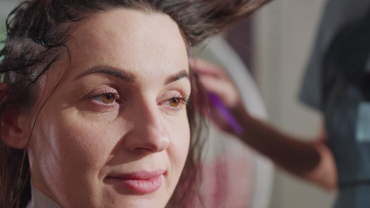 Auftragen von Haarfärbemittel, ein erfahrene/r StylistIn trägt eine lebendige Haarfarbe auf, ein/e erfahrene/r KosmetikerIn färbt das Haar sorgfältig im Salon, ein/e professionelle/r ColoristIn trägt aufmerksam eine Nuance in einladender Atmosphäre auf