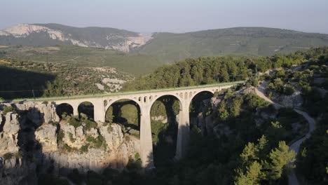 Historical-stone-bridge,-Drone-view-of-a-historical-stone-bridge-built-over-the-river-covered-with-greenery