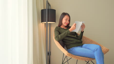 Young-adult-Asian-woman-with-casual-clothes-sitting-on-Rattan-lounge-chair-with-reading-a-book