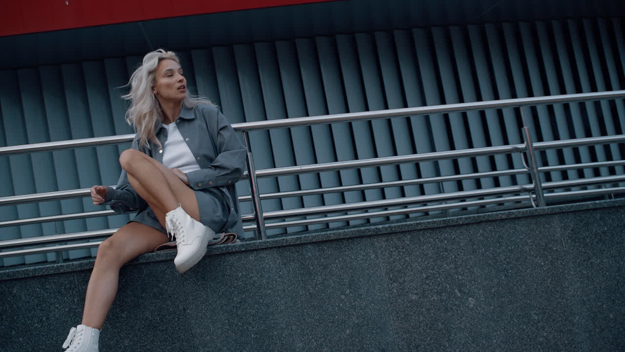 модная женщина, моделирующая городской фон, сидит на здании.