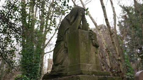 praying statue on a gravestone covered in moss in a forest cemetery on a cloudy day