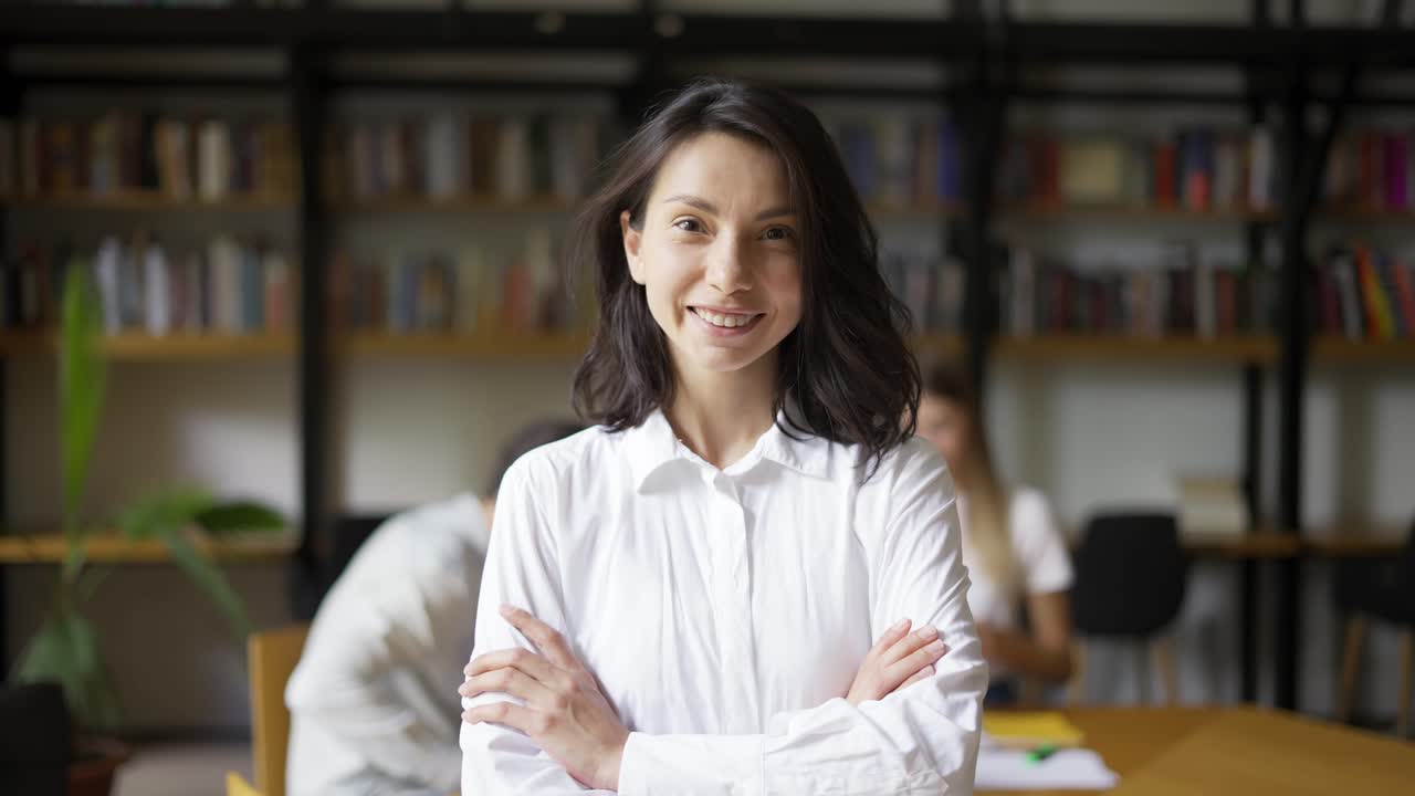 chica linda positiva con cabello negro con camisa estudiante o maestro mirando a la cámara sonriendo amistosamente