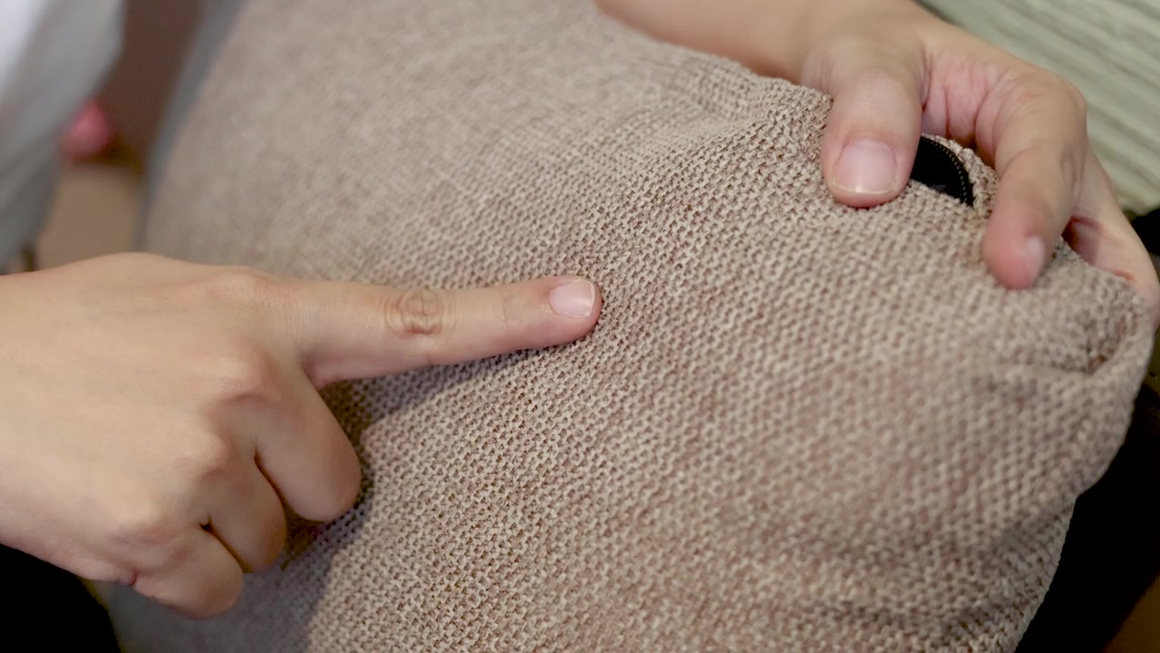 Close-up shot of hands pointing at the textured fabric of a beige linen cushion
