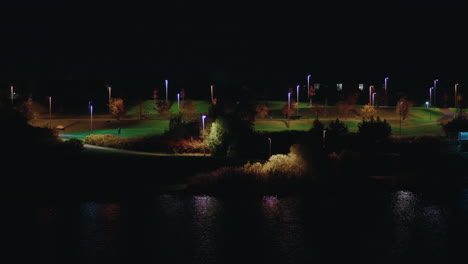 person walking at pae park alongside pond illuminated with night light, tallinn, estonia