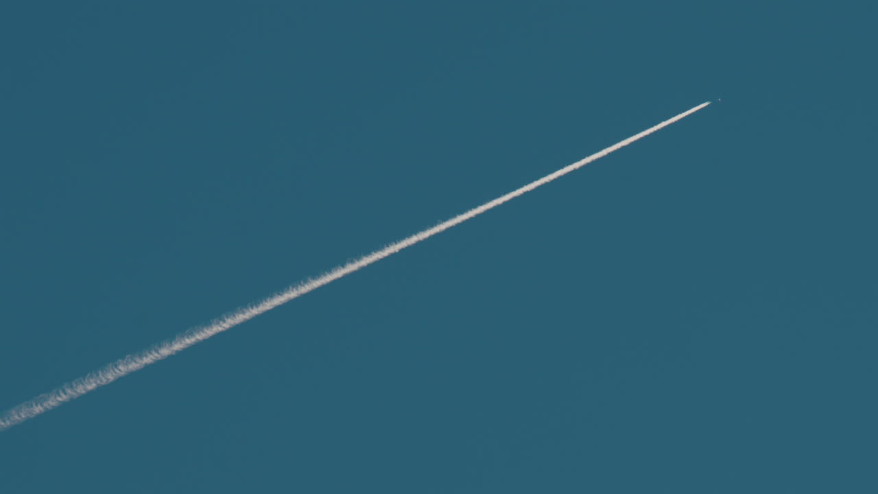 Airplane flying high above leaving long contrails in a clear blue sky