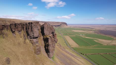 borde escarpado del acantilado con vistas a vastos campos agrícolas verdes bajo un cielo azul claro en islandia, vista aérea