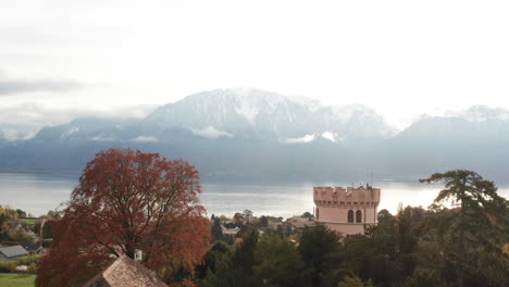 flying between tree and building, revealing beautiful swiss town with a lake and mountain in the background