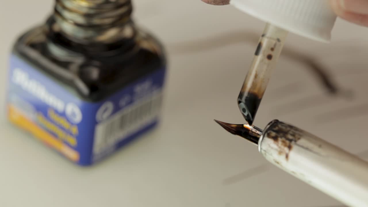 Close-up of a fountain pen being filled with black ink from a bottle, focus on nib