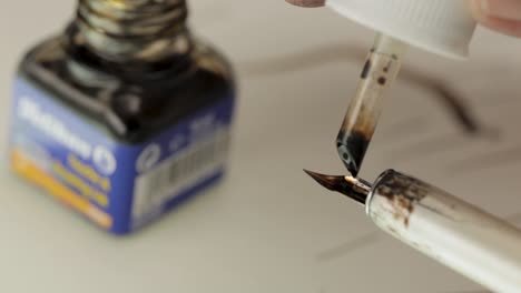 Close-up-of-a-fountain-pen-being-filled-with-black-ink-from-a-bottle,-focus-on-nib