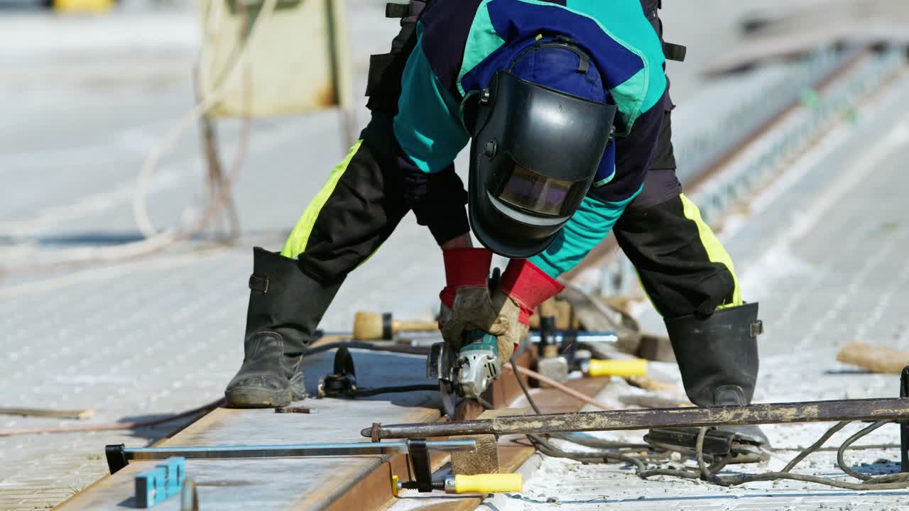 Man in safety gear working on railway track with power grinder in slow motion