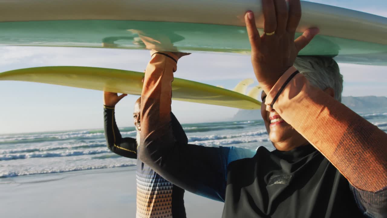Senior african american couple walking with surfboards at the beach