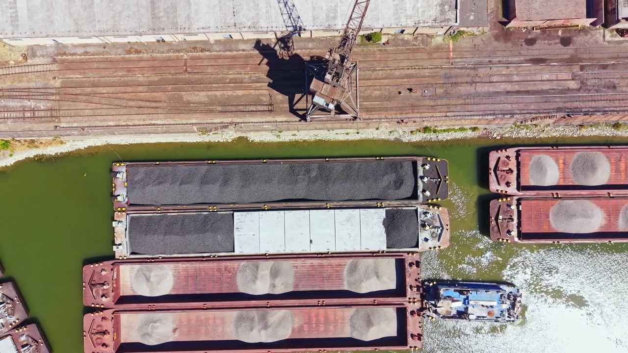 Chiatte da carico cariche di merci navigano attraverso un canale trafficato vicino a una zona industriale in una giornata di sole in città