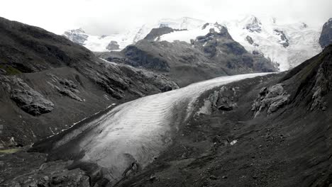 Aerial-flyover-towards-the-end-of-Morteratsch-glacier-in-Engadin,-Switzerland-with-some-of-the-tallest-peaks-of-the-Swiss-Alps-like-Piz-Bernina,-Piz-Palu-hidden-in-the-clouds