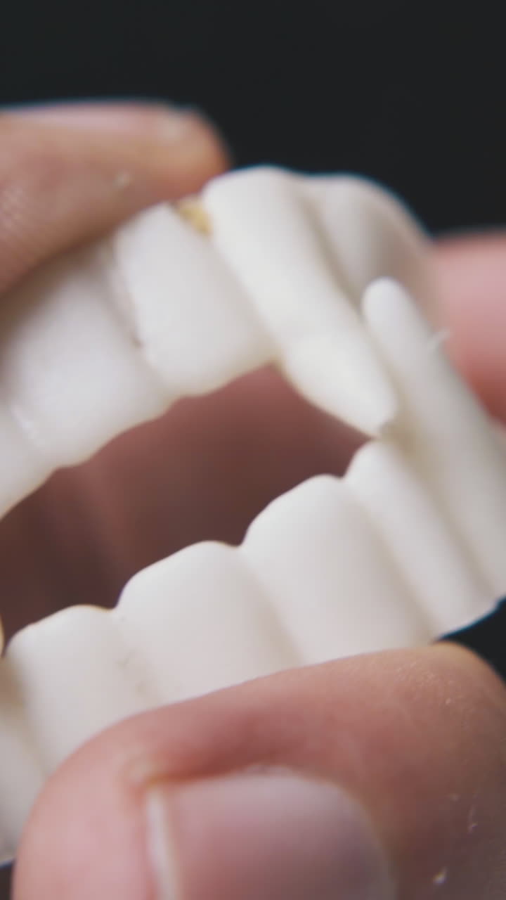 young person plays with funny white plastic toy vampire teeth on black background extreme close view