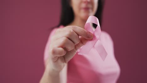 Mid-section-of-woman-holding-a-pink-ribbon-against-pink-background