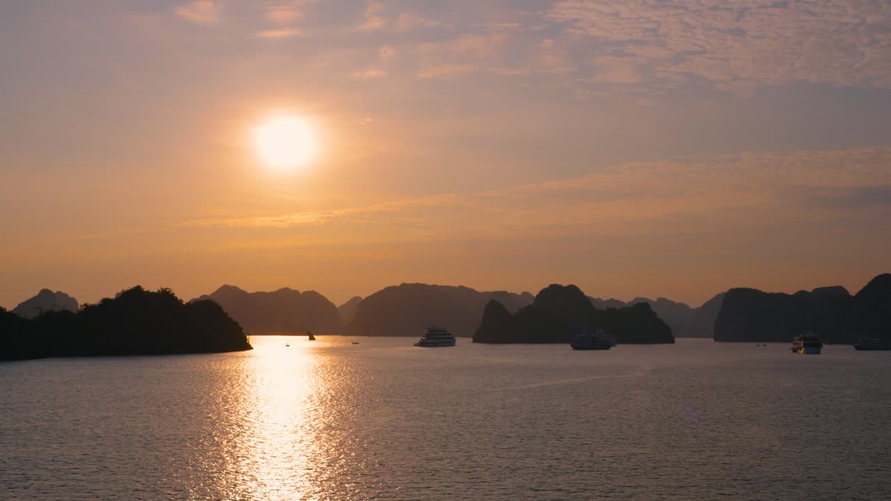 Aerial panning shot of silhouetted cruising ships in Ha Long Bay with a beautiful sunset and island cliffs in the background