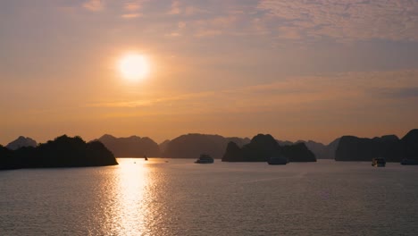 aerial panning shot of silhouetted cruising ships in ha long bay with a beautiful sunset and island cliffs in the background