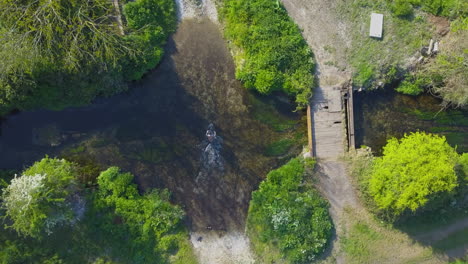 Mountain-biker-riding-through-river,-aerial-top-down-view-of-adventure