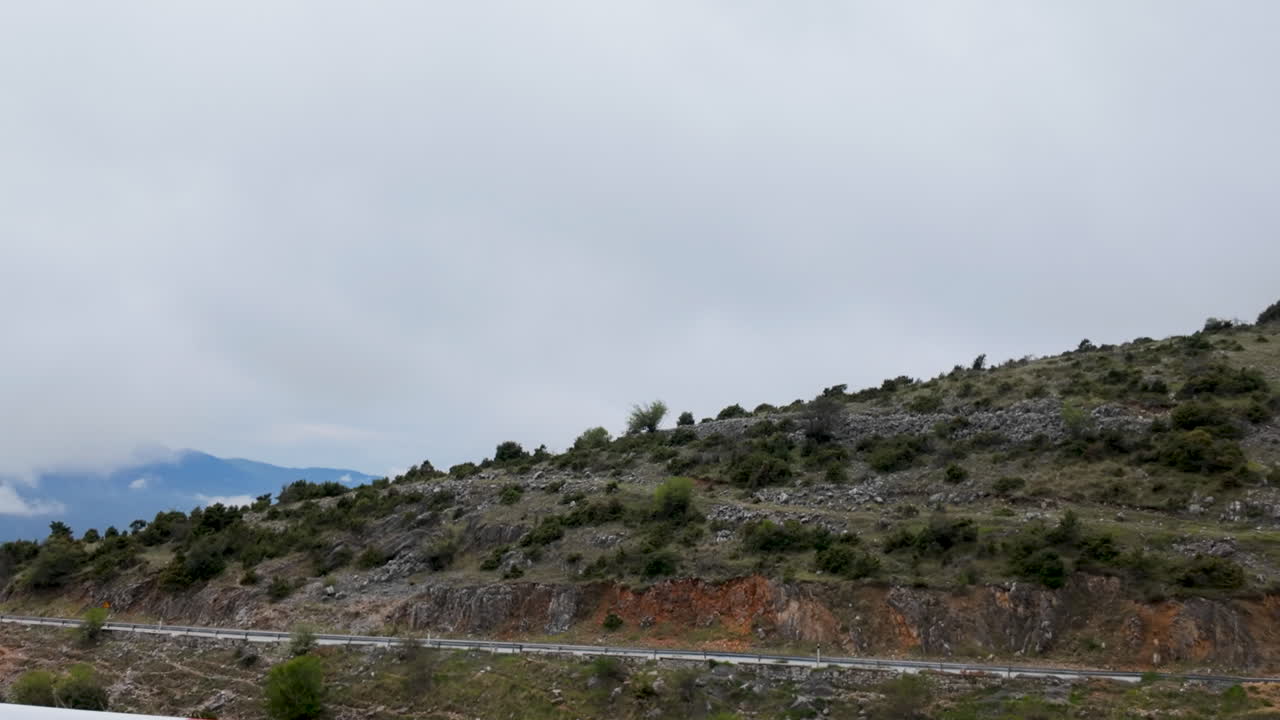 Vista panoramica di una strada asfaltata tortuosa che attraversa le montagne rocciose greche in una giornata nuvolosa, ideale per contenuti di viaggio e automobilistici