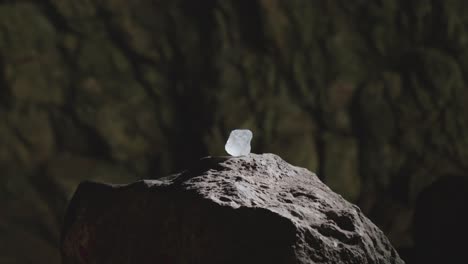 cinematic shot of a luminous raw crystal resting on a rock pedestal in a dark cave. mysterious smoke drifts by, creating a magical or sacred fantasy atmosphere