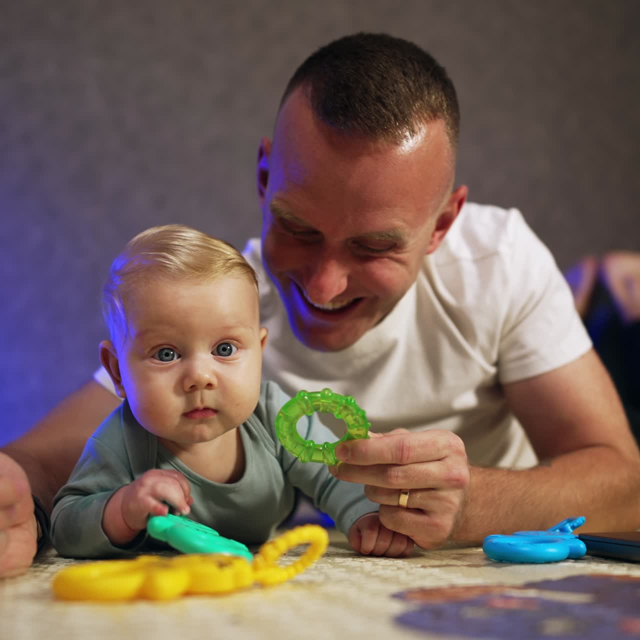 Father and infant son spending time together at home. Man with a baby lies on the floor giving toys to his kid. Close up