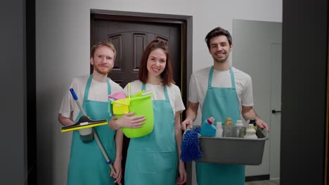 Retrato-De-Un-Trío-De-Limpiadores-Profesionales-Con-Un-Delantal-Azul-Y-Varios-Artículos-De-Limpieza,-Limpiador-Y-Trapeador-En-Un-Apartamento-Moderno,-Limpieza-De-Guardia