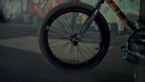 Bmx-bicycle-wheel-spinning-at-skatepark-with-graffiti-wall.-Bike-parking.