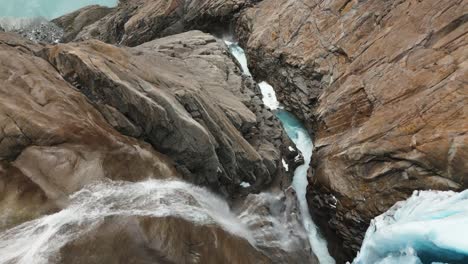 a-waterfall-of-a-glacier-falls-down-between-rocks,-Briksdalsbreen,-norway,-nature,-drone