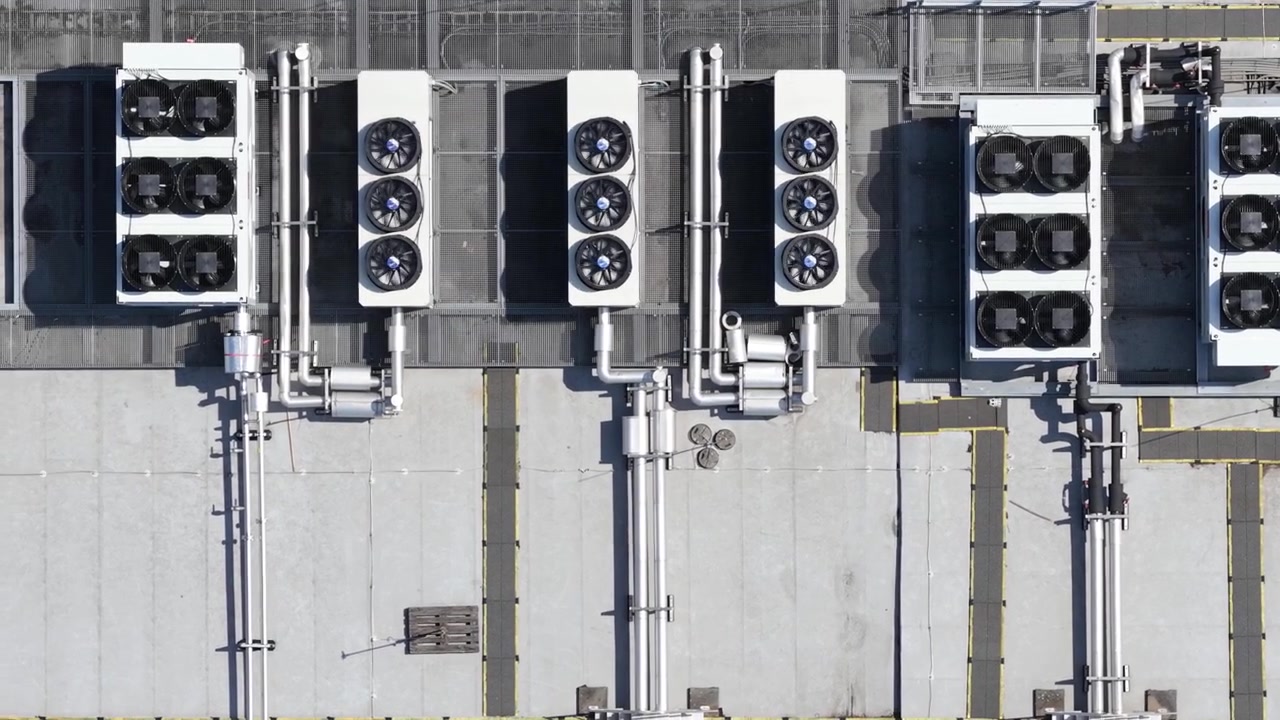 Top down aerial view of large industrial hvac air conditioning units installed on the flat roof of a modern building, showing ventilation fans spinning and complex piping systems